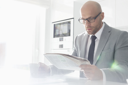 Mid adult businessman having coffee while reading newspaper at homeの写真素材
