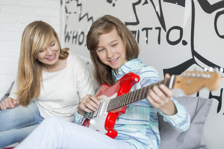 Girl listening to sister playing guitar at homeの写真素材