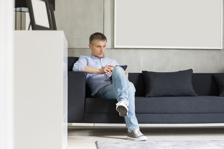 Full-length of Middle-aged man using digital tablet on sofaの写真素材