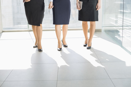 Low section of businesswomen standing on tiled floor in officeの写真素材