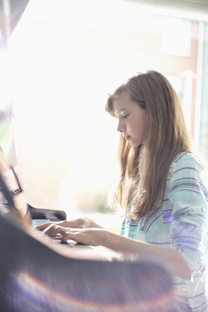 Side view of girl playing piano at homeの写真素材