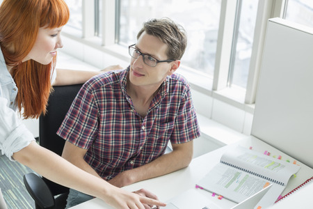 Business couple looking at each other while using laptop in creative officeの写真素材