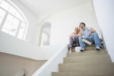 Low angle view of couple with painting tools sitting on steps in new houseの写真素材