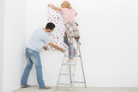 Full-length rear view of couple applying wallpaper to wallの写真素材