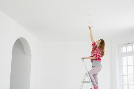 Full-length of woman on ladder fitting light bulb in new houseの写真素材