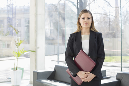 Portrait of businesswoman holding file while standing at office lobbyの写真素材