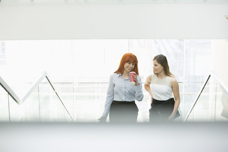 Businesswomen having coffee while moving up steps in officeの写真素材