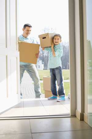Happy father and son with cardboard boxes entering into new houseの写真素材
