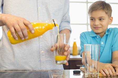 Midsection of father serving orange juice for son in kitchenの写真素材