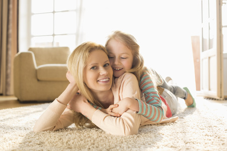 Portrait of happy mother with daughter lying on floor at homeの写真素材