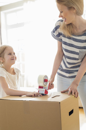 Mother and daughter looking at each other while packing cardboard box at homeの写真素材