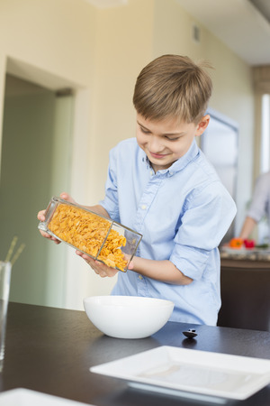 Smiling boy pouring corn flakes in bowl at homeの写真素材