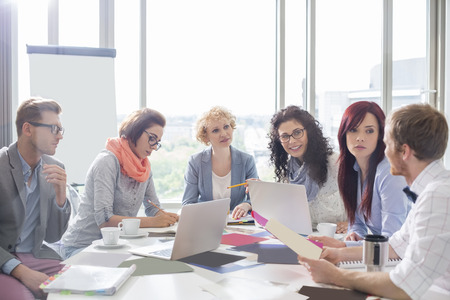 Business colleagues discussing over photographs at conference table in creative officeの写真素材