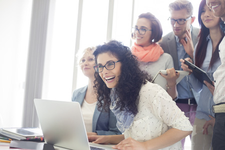 Group of cheerful businesspeople with laptop at desk in creative officeの写真素材