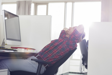 Side view of young businessman relaxing at computer desk in officeの写真素材