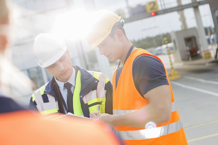 Male workers discussing over clipboard in shipping yardの写真素材