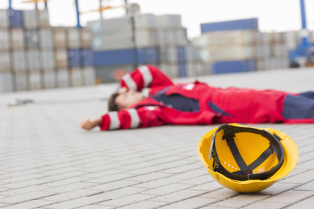 Yellow hardhat at shipyard with depressed male worker lying in shipping yardの写真素材