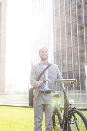 Happy businessman standing with bicycle outside buildingの写真素材