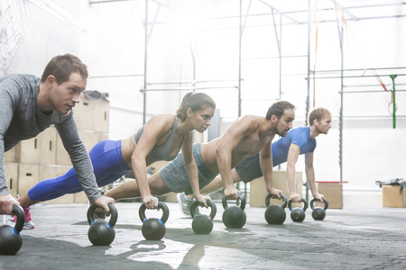 Dedicated people doing pushups with kettlebells at crossfit gym