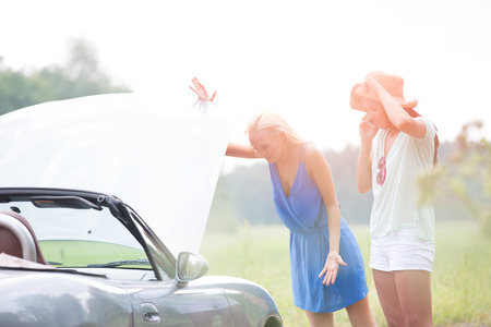 Worried female friends examining broken down car on sunny dayの写真素材