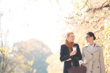 Happy businesswomen conversing while walking at park on sunny dayの写真素材