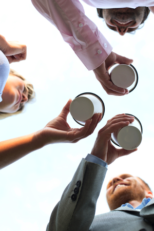 Directly below shot of businesspeople holding disposable cups against clear skyの写真素材
