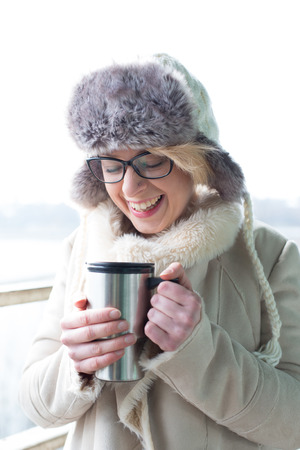 Cheerful woman in warm clothing holding insulated drink containerの写真素材