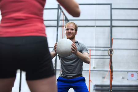 Happy man throwing medicine ball towards woman in crossfit gym