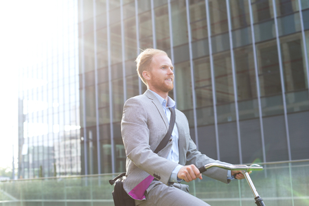Businessman riding bicycle outside office buildingの写真素材