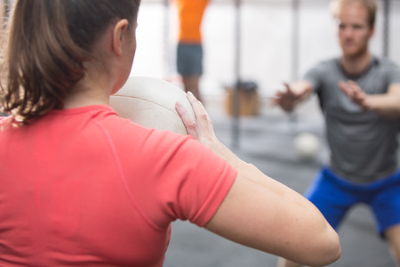 Rear view of woman throwing medicine ball towards man in crossfit gym
