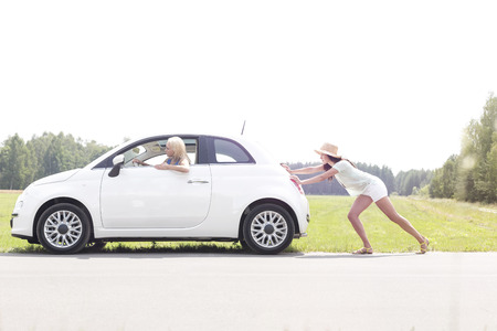 Woman pushing broken down car on country roadの写真素材