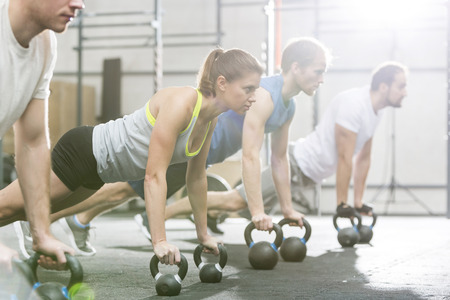 Determined people doing pushups with kettlebells at crossfit gymの写真素材