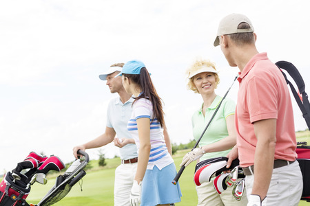 Friends talking while walking at golf course against clear skyの写真素材