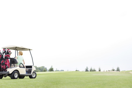 Couple sitting in golf cart against clear skyの写真素材