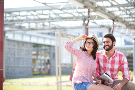 Happy couple looking away while sitting on bench under shadeの写真素材
