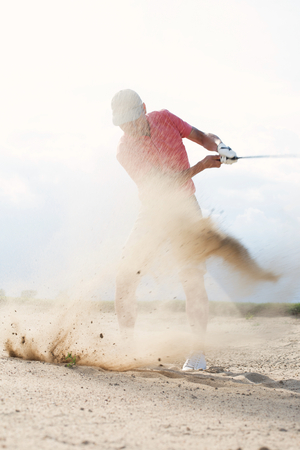 Middle-aged man splashing sand while playing at golf courseの写真素材