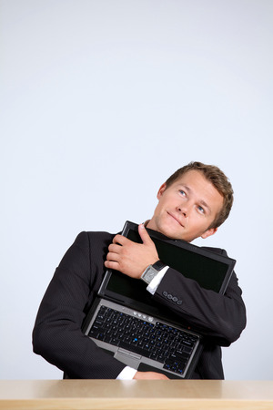 Businessman embracing laptop, looking upの写真素材