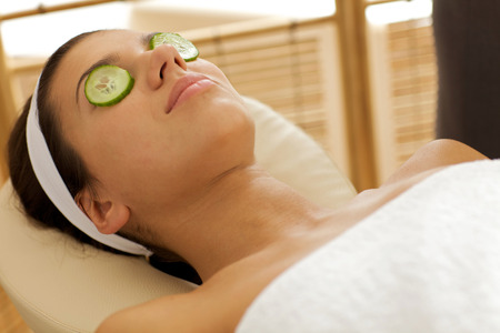 Young woman lying down in massage table with cucumbers on eyesの写真素材