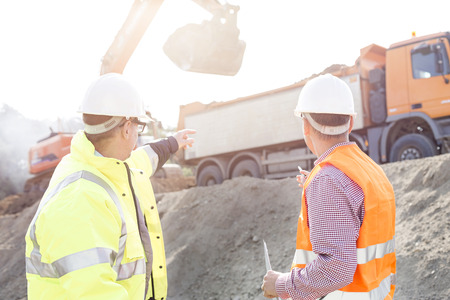 Engineer pointing at vehicles while discussing at construction siteの写真素材