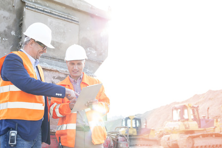 Happy supervisors discussing over clipboard at construction site against clear sky