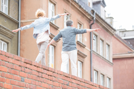 Rear view of middle-aged couple with arms outstretched walking on brick wallの写真素材