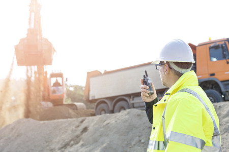 Side view of supervisor using walkie-talkie at construction site against clear skyの写真素材