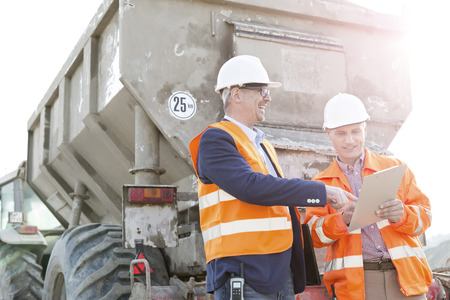 Happy architects discussing over clipboard by construction truckの写真素材