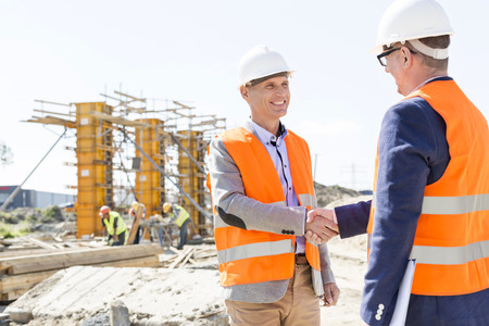 Engineers shaking hands at construction site against clear skyの写真素材