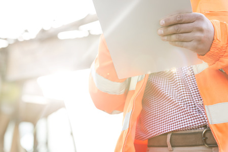 Midsection supervisor holding clipboard at construction site on sunny dayの写真素材