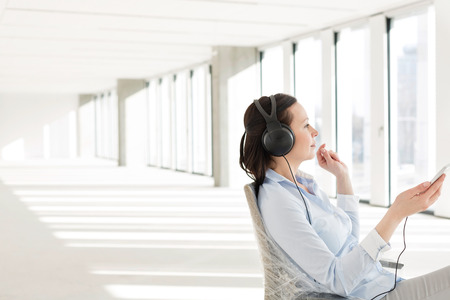 Side view of mid adult businesswoman listening music through headphones in empty officeの写真素材