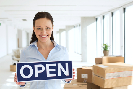 Portrait of smiling mid adult businesswoman holding open sign in new office