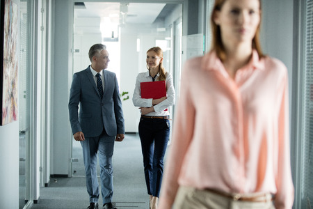 Businessman and businesswoman talking while walking in office corridor with female colleague in foregroundの写真素材