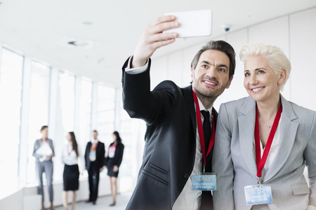 Business people taking selfie in convention center with colleagues walking in backgroundの写真素材