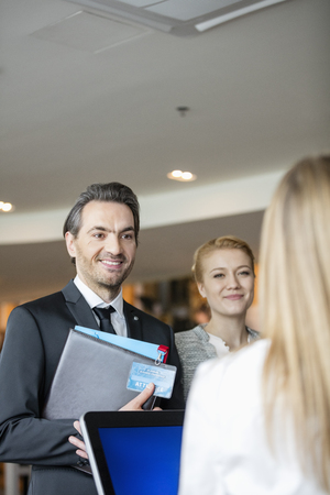 Smiling business people looking at receptionist in convention centerの写真素材